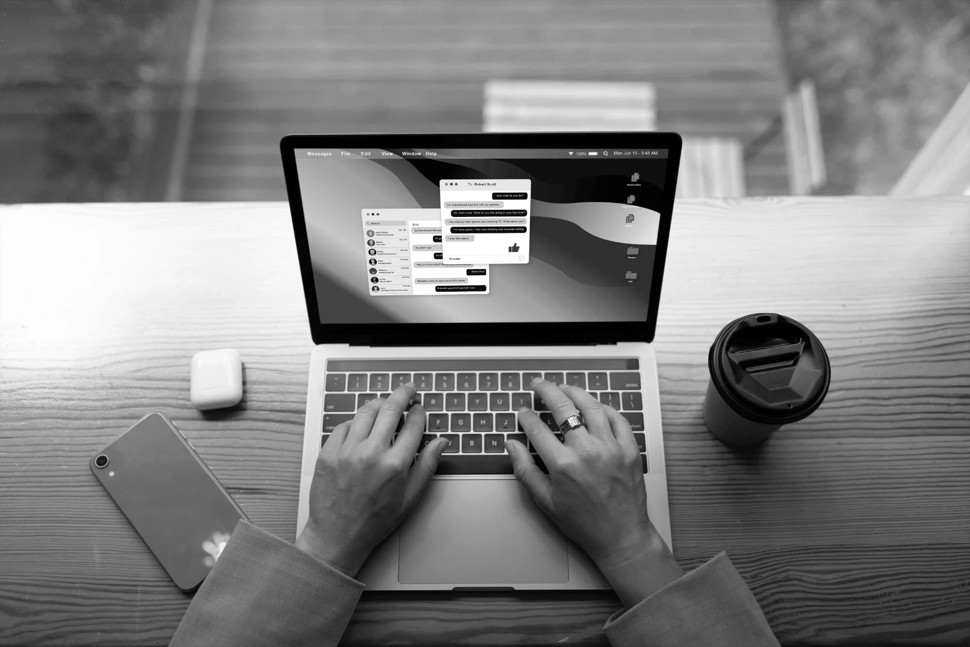Overhead view of hands typing on a laptop showing a messaging app, beside a phone, earbuds and a coffee cup
